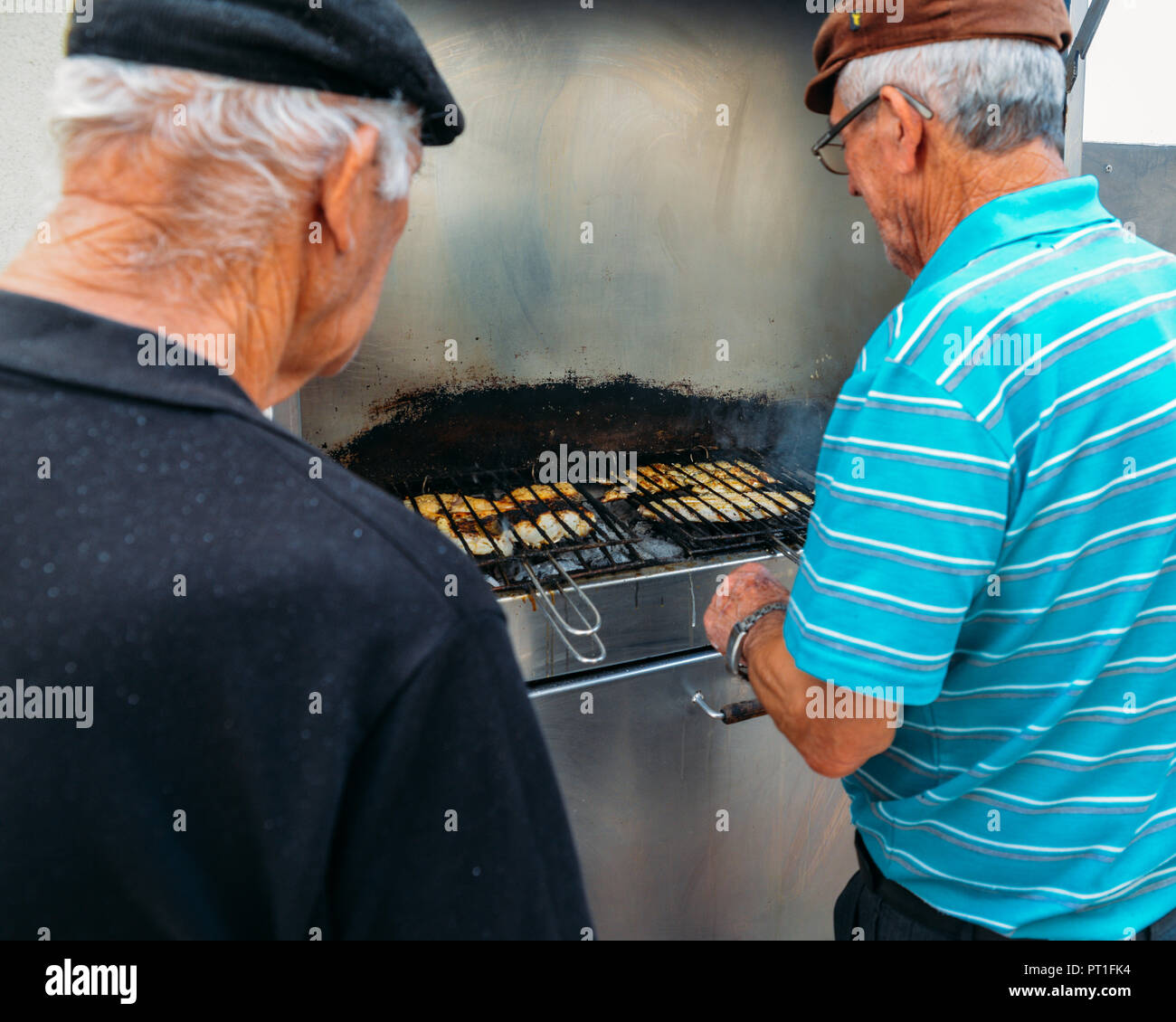 Nazare, Portugal - Sept 25, 2018: Zwei portugiesische Männer BBQ frische Fische, darunter auch den berühmten Bacalhau, auf einem Grill in der Küstenstadt Nazare, Portugal Stockfoto