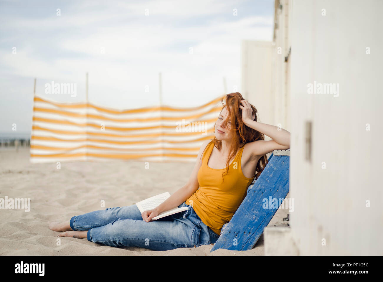 Rothaarige Frau vor der Hütte am Strand sitzen, ein Buch lesen Stockfoto
