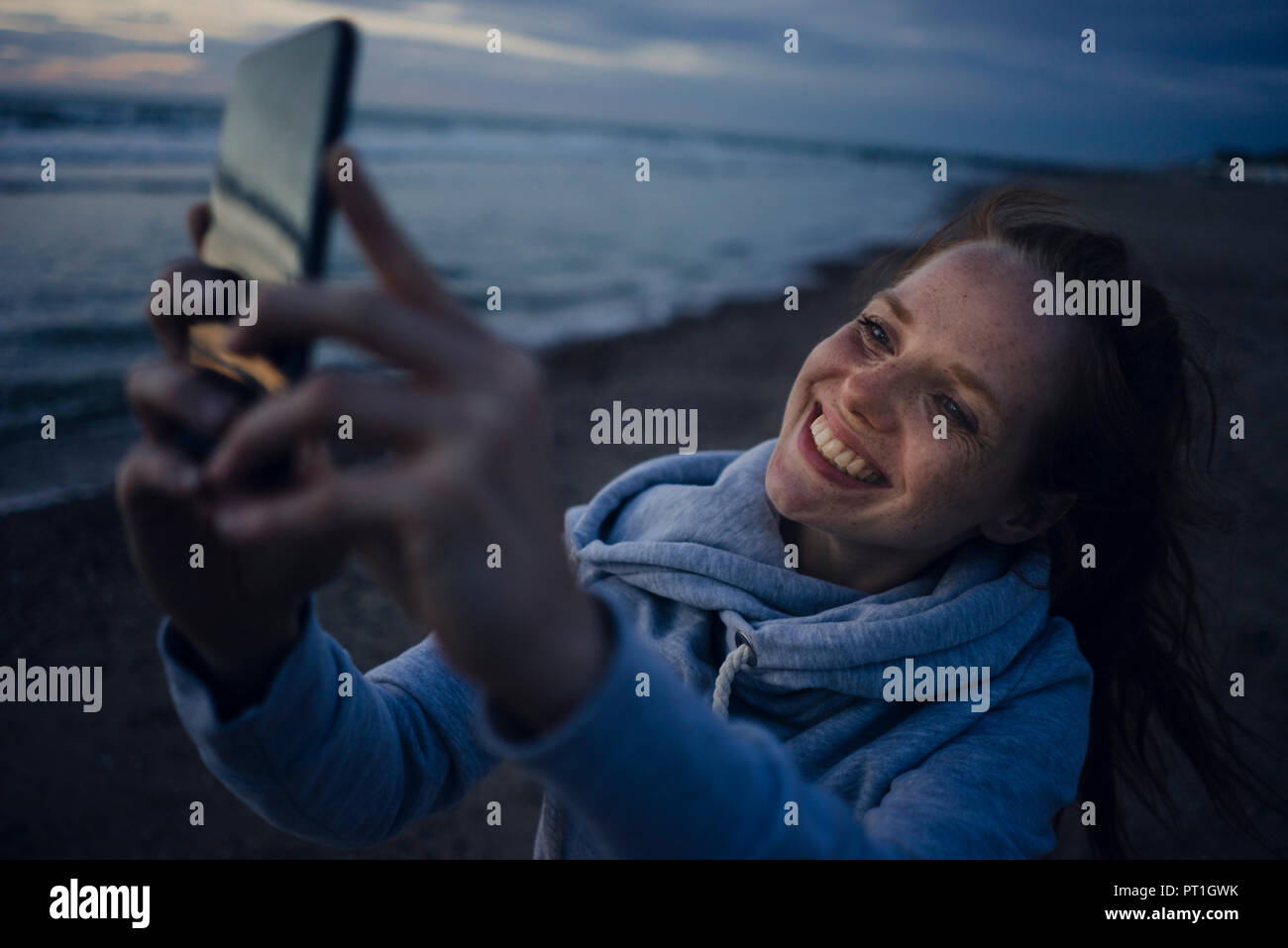 Frau mit Smartphone auf dem Strand bei Sonnenuntergang Stockfoto