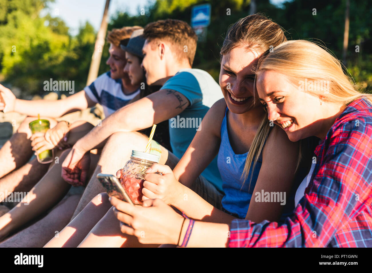 Gruppe der glücklichen Freunde sitzen im Freien mit erfrischenden Getränken und Mobiltelefone Stockfoto