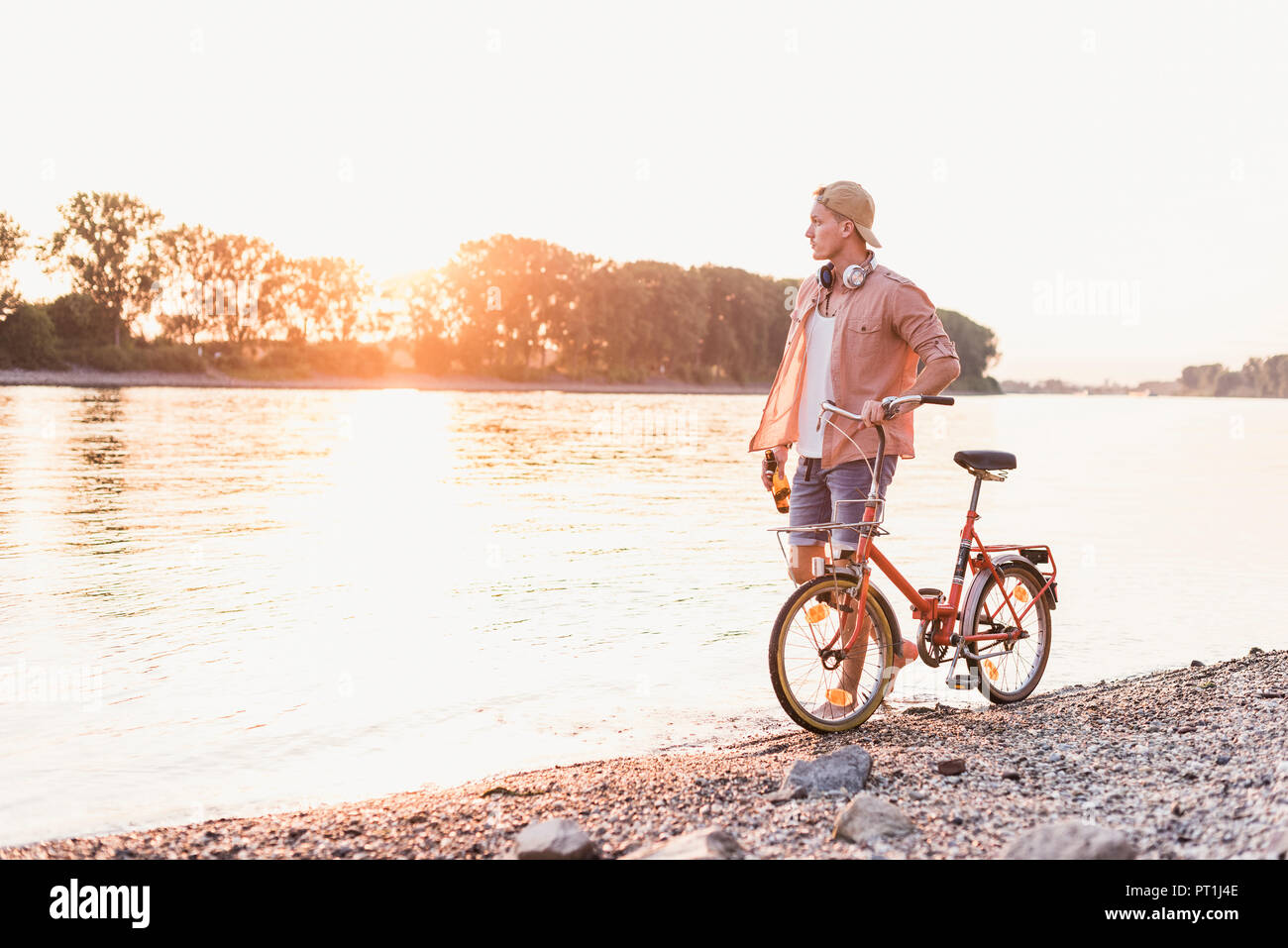 Junger Mann zu Fuß mit dem Fahrrad am Ufer bei Sonnenuntergang Stockfoto