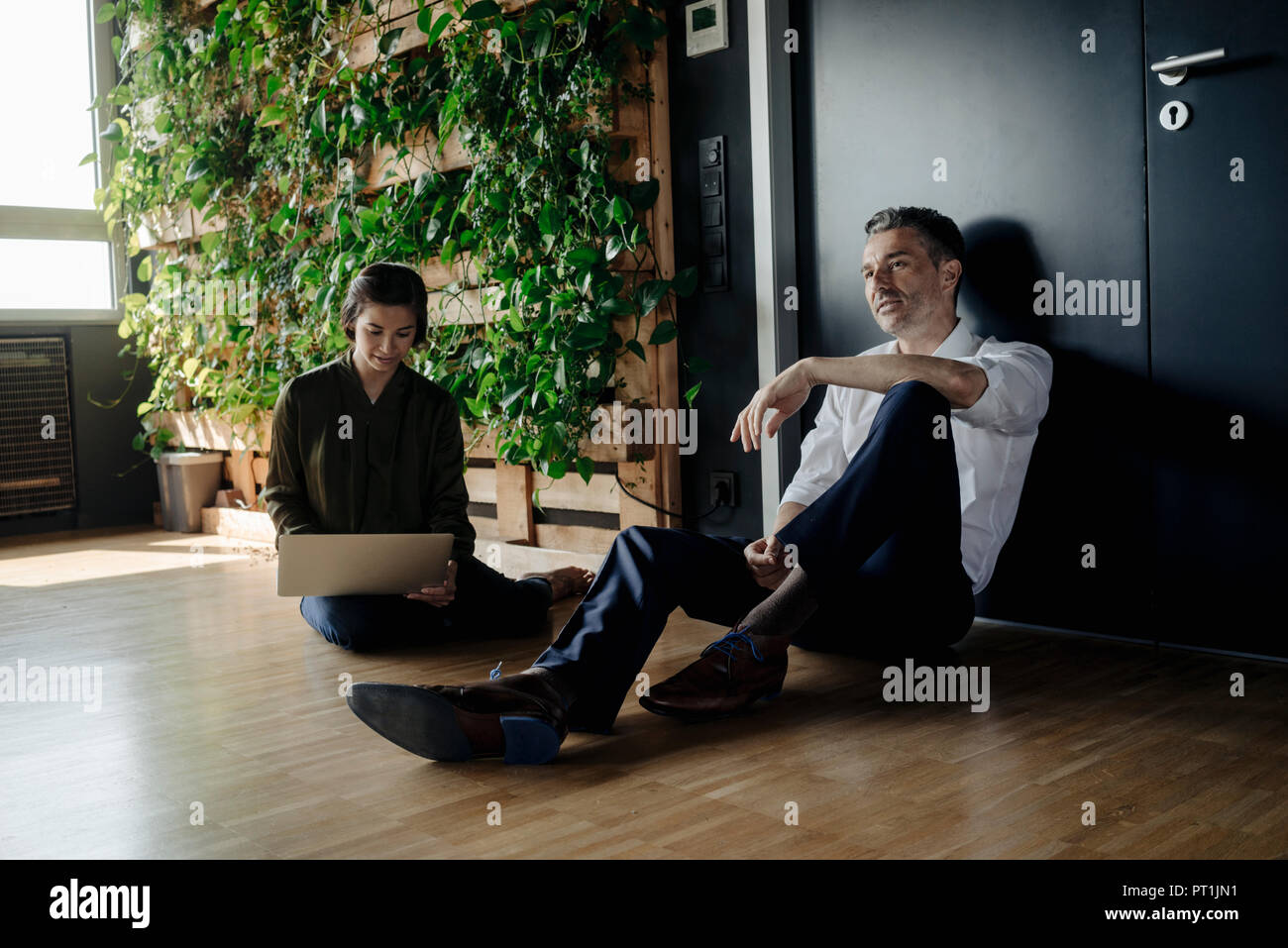 Geschäftsmann und Geschäftsfrau, sitzen auf dem Boden in Green Office mit Tablet Stockfoto