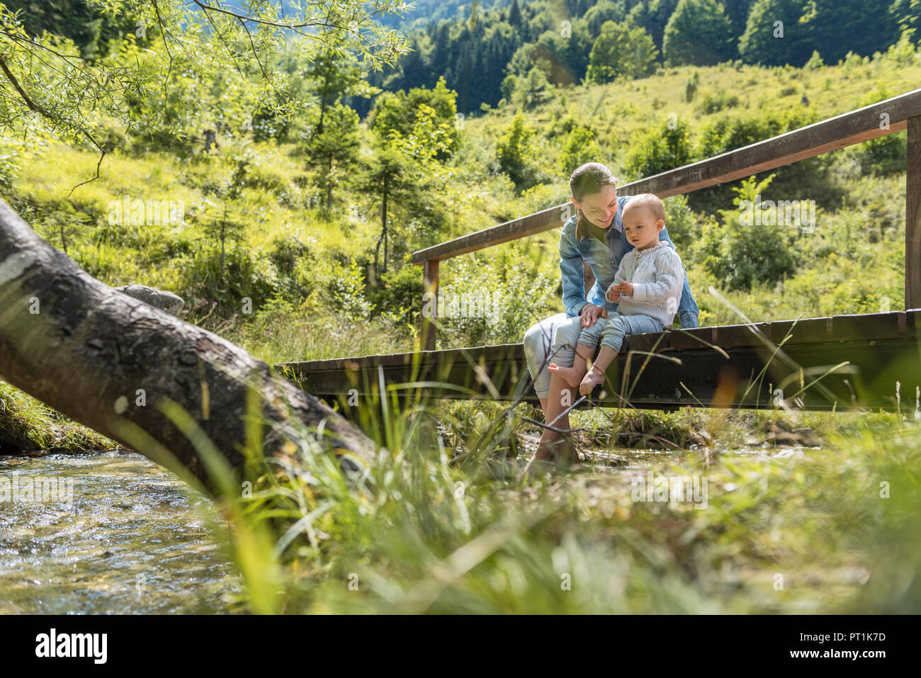 Mutter und Tochter sitzen auf Holzbrücke, Mountain Stream Stockfoto