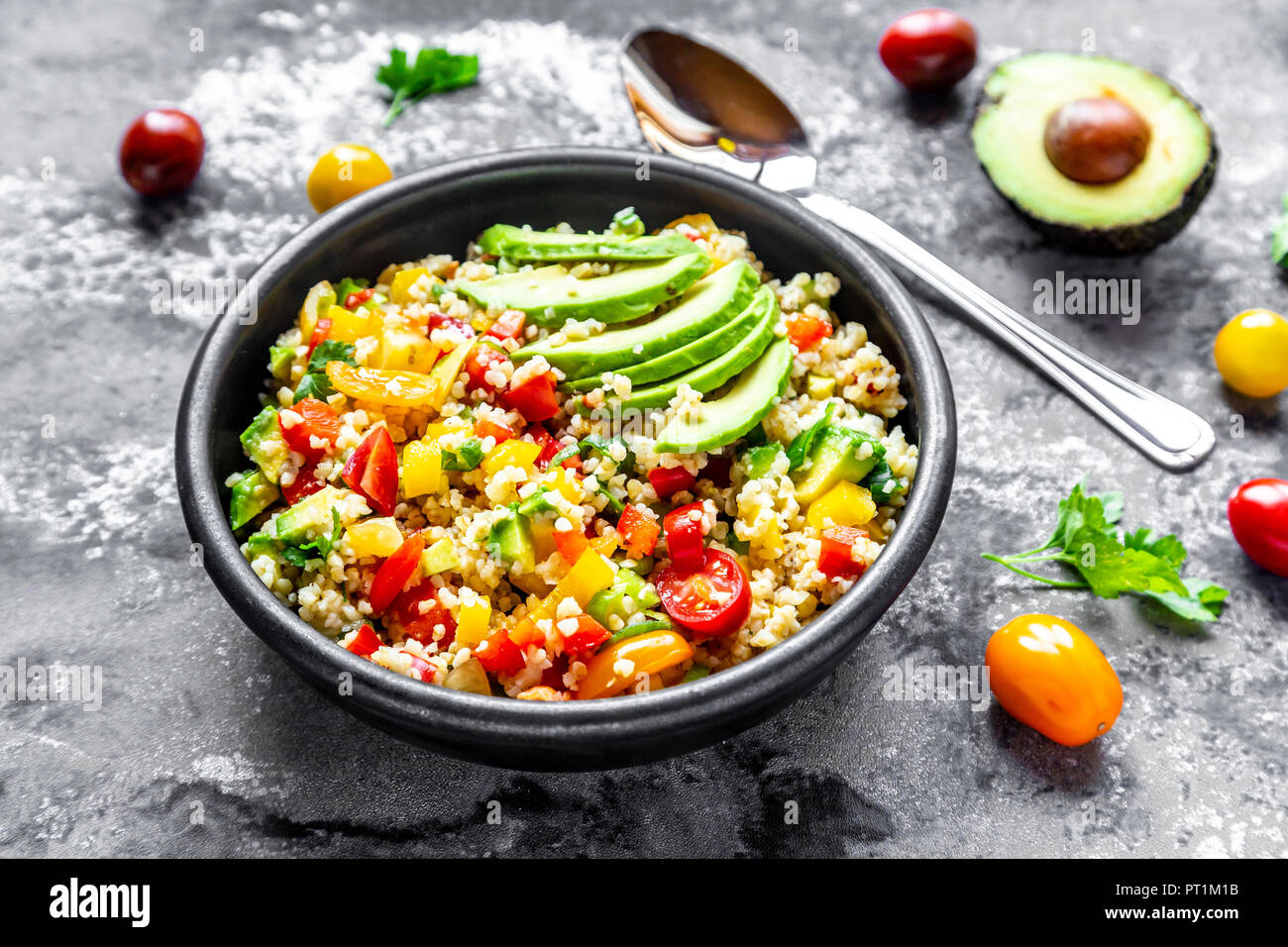 Schüssel mit Bulgur Salat mit Paprika, Tomaten, Avocado, Frühlingszwiebeln und Petersilie Stockfoto