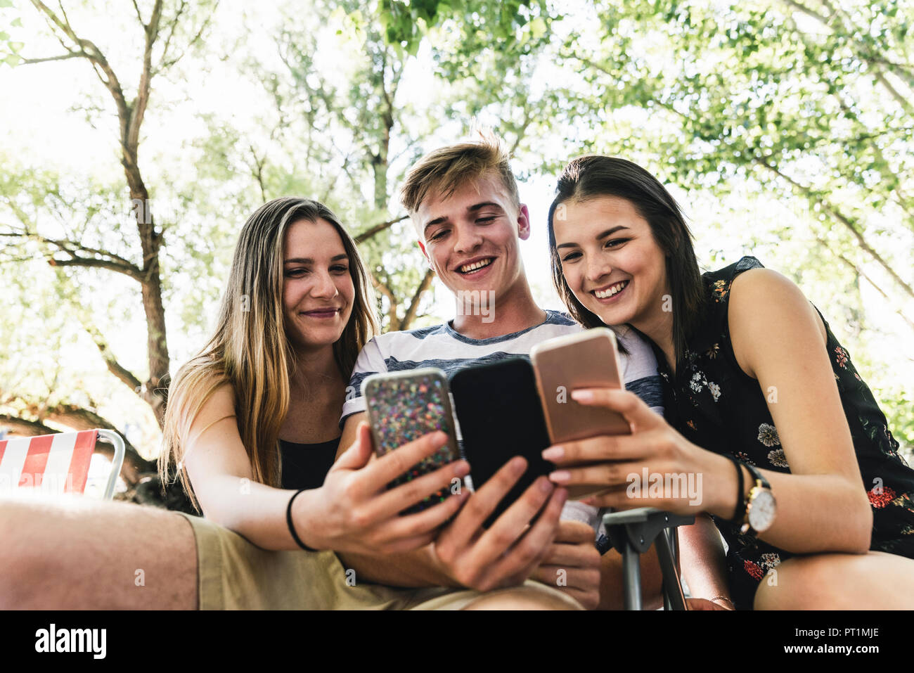 Drei glückliche Freunde auf der Suche nach Handys im Freien Stockfoto