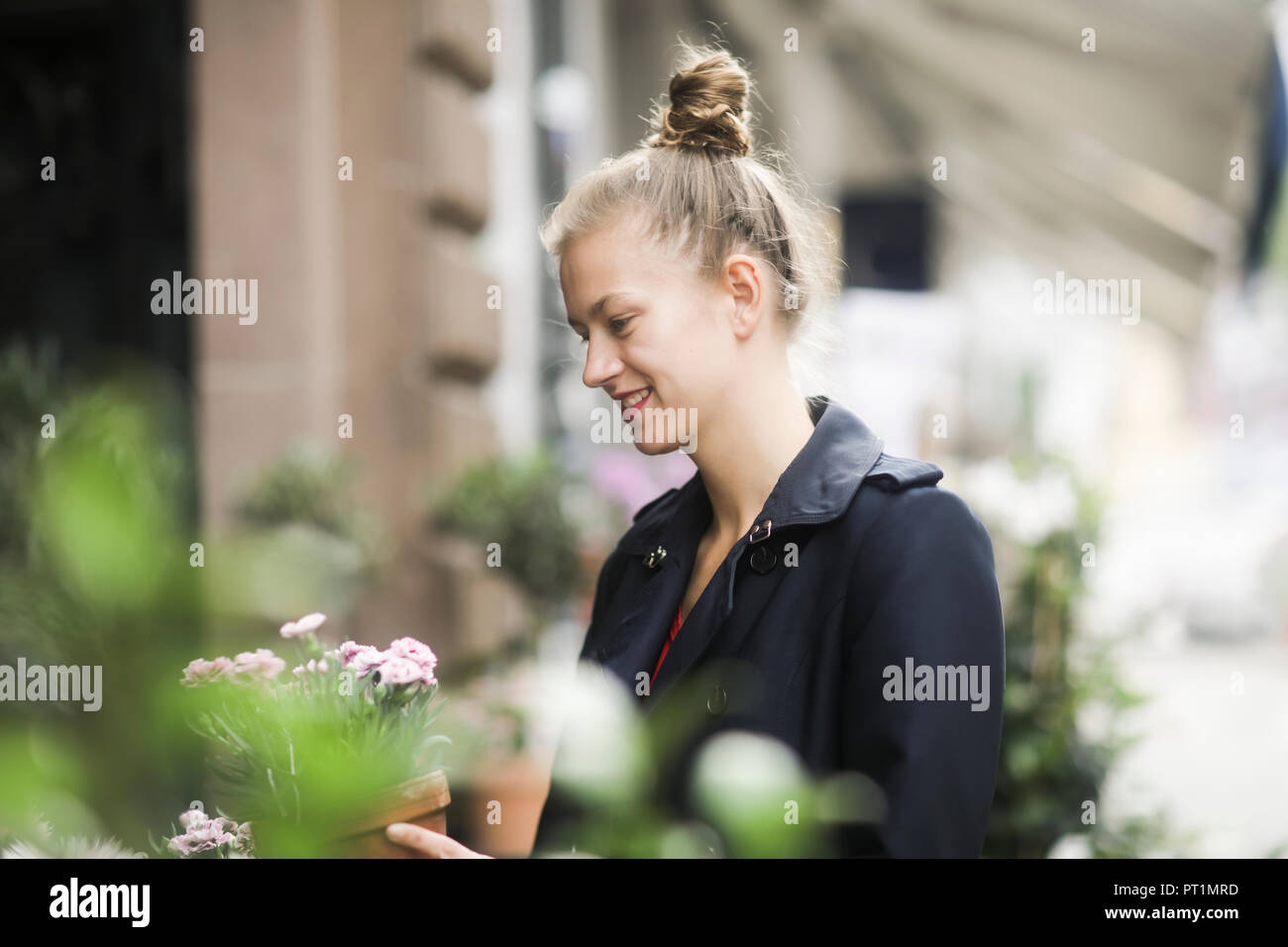 Lächelnden jungen Frau Wahl Topfpflanze vor einem Blumenladen Stockfoto