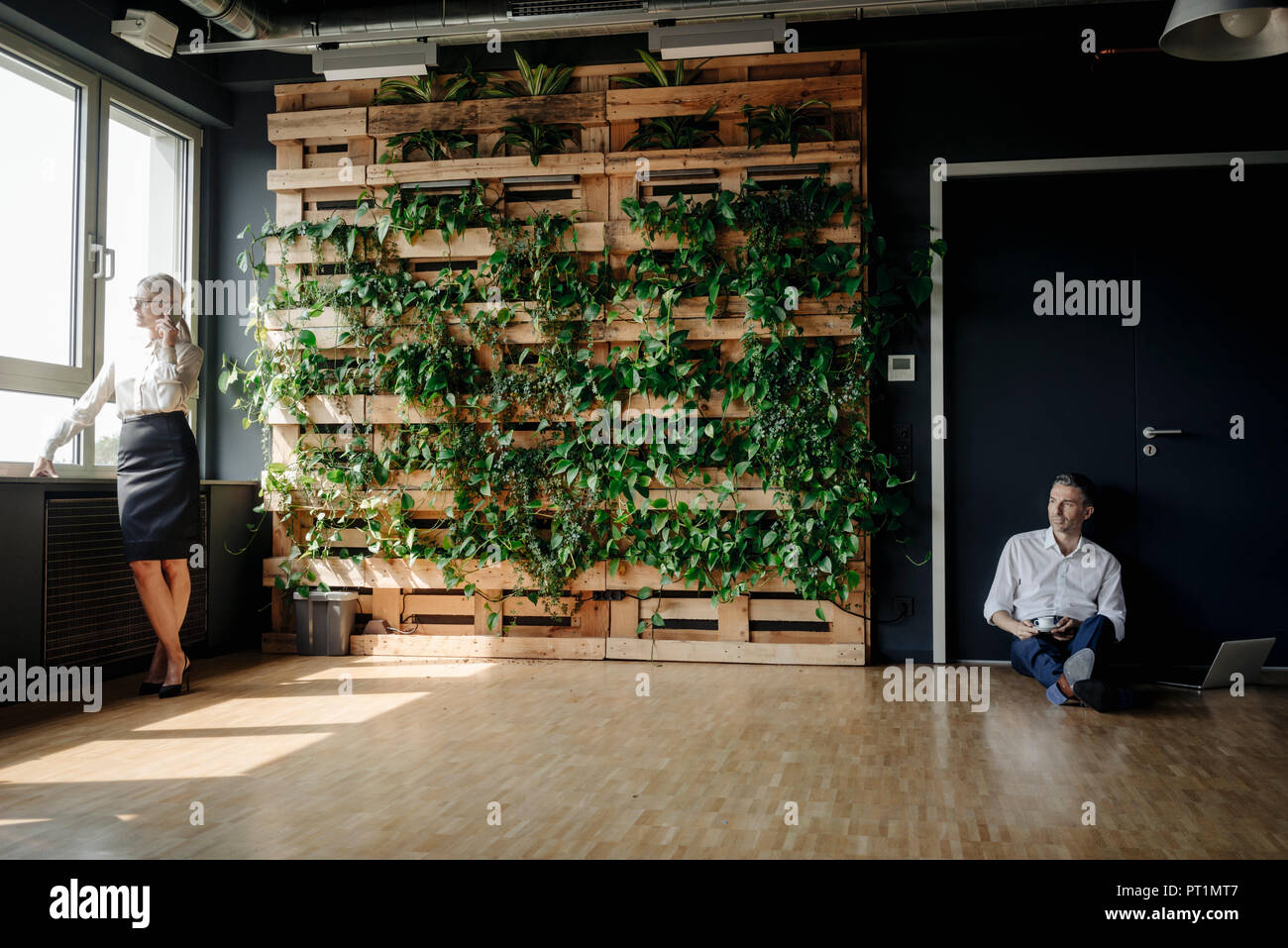 Unternehmer sitzen und Geschäftsfrau auf Handy in Green Office Stockfoto