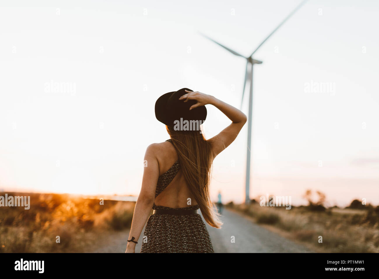 Zurück Blick auf die junge Frau auf die ländliche Straße in den Abend mit Windrad im Hintergrund Stockfoto