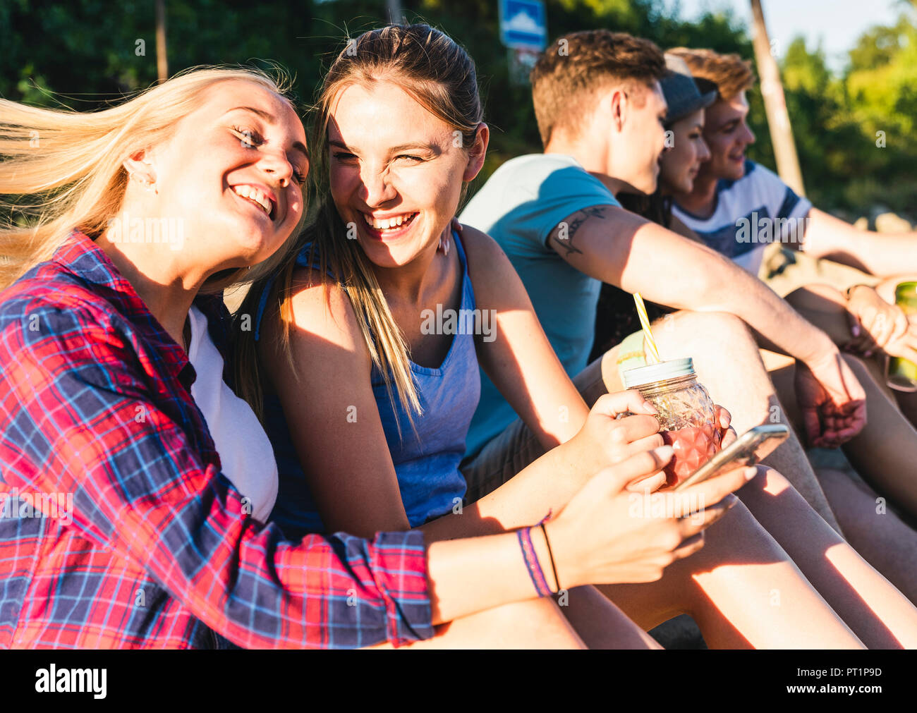 Gruppe der glücklichen Freunde sitzen im Freien mit erfrischenden Getränken und Mobiltelefone Stockfoto
