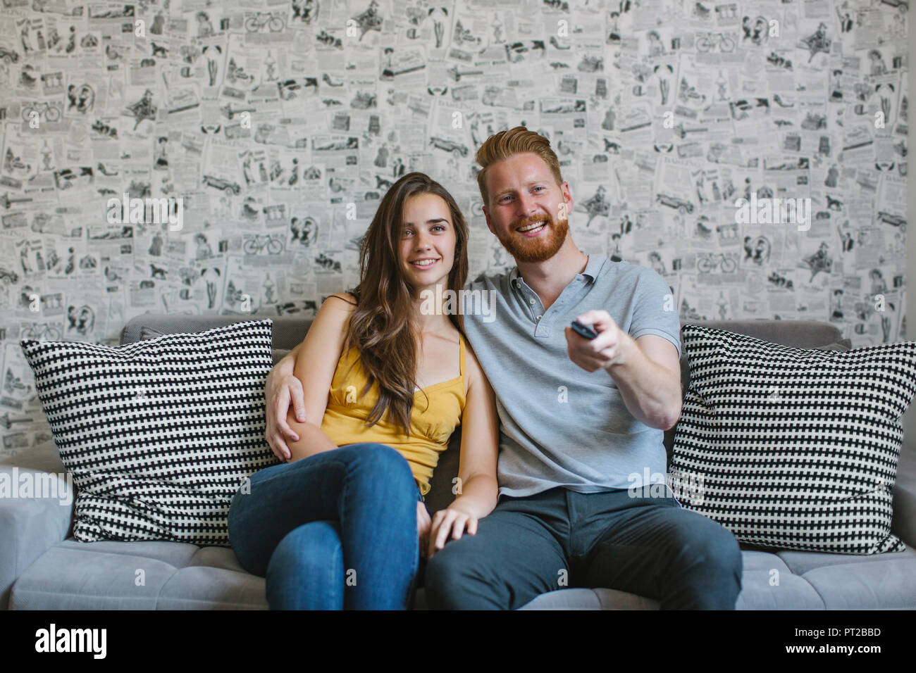 Lächelndes Paar sitzt auf der Couch vor dem Fernseher Stockfoto