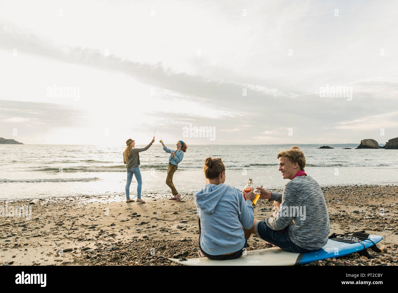 Gerne Freunde mit Surfbrett und Getränke am Strand bei Sonnenuntergang Stockfoto