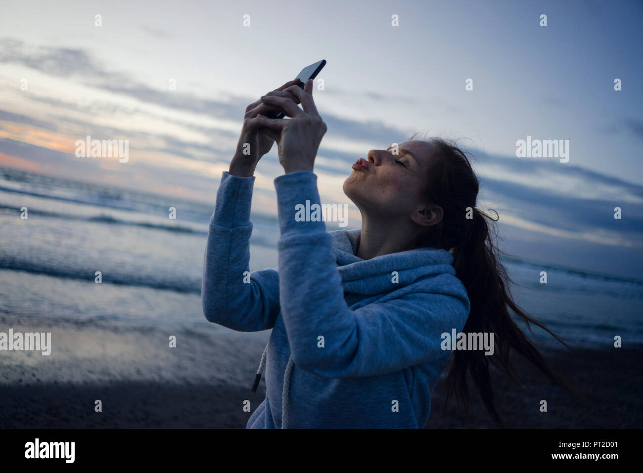 Frau mit Smartphone auf dem Strand bei Sonnenuntergang, senden Kiss Stockfoto