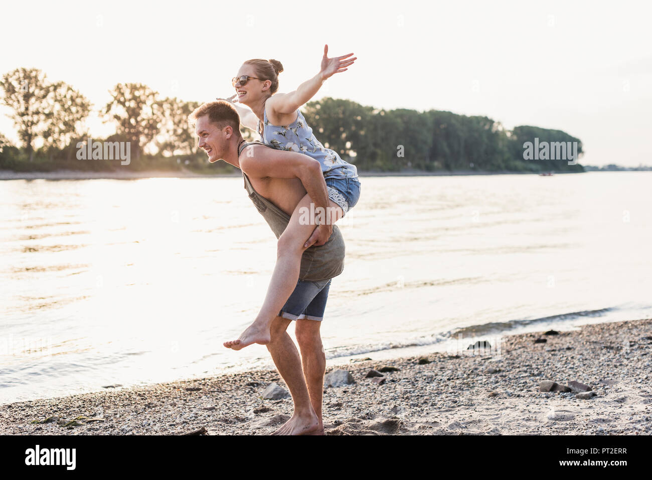 Junger Mann, Freundin piggyback Ride am Flussufer Stockfoto