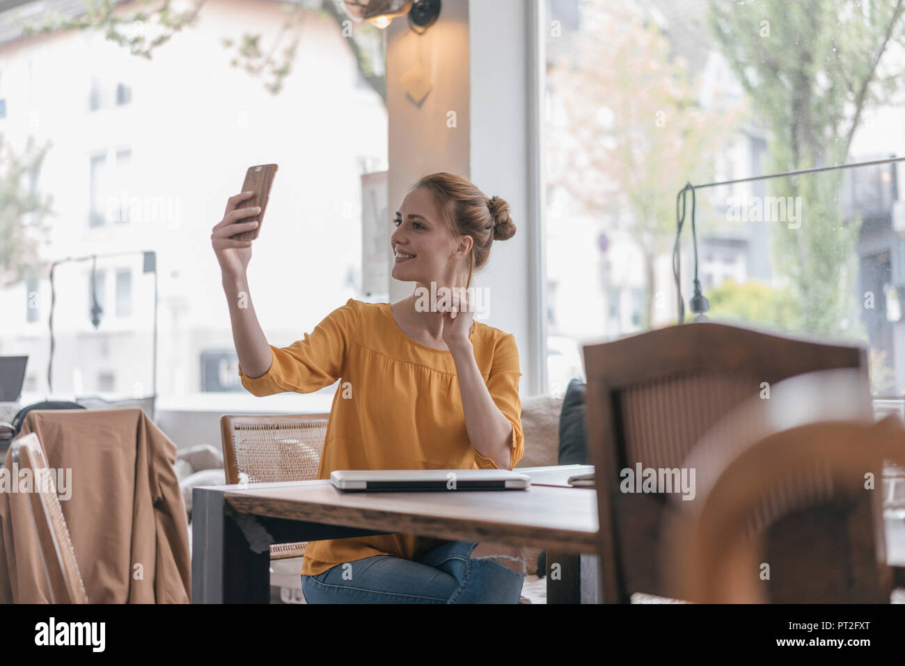Junge Frau sitzt im Coworking Space, Smartphone selfie Stockfoto