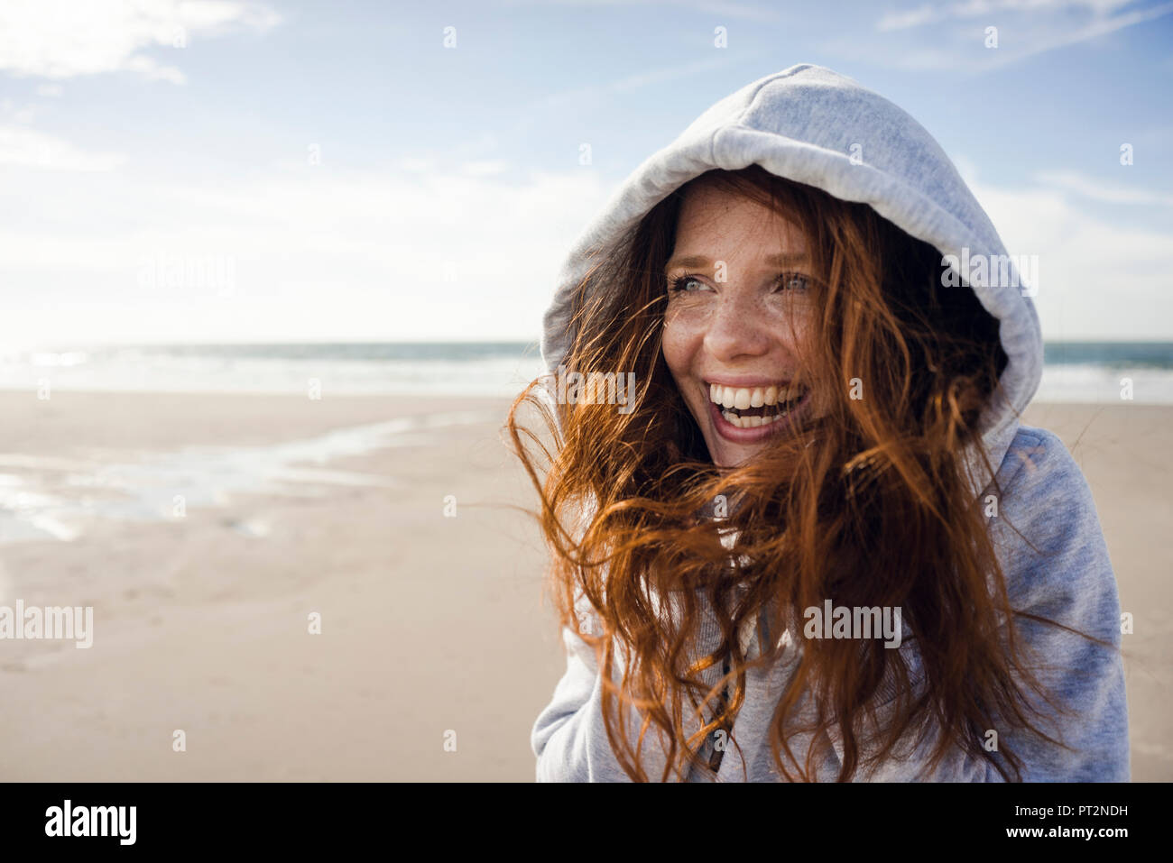 Frau Spaß zu haben an einem windigen Strand, mit Haube Stockfoto