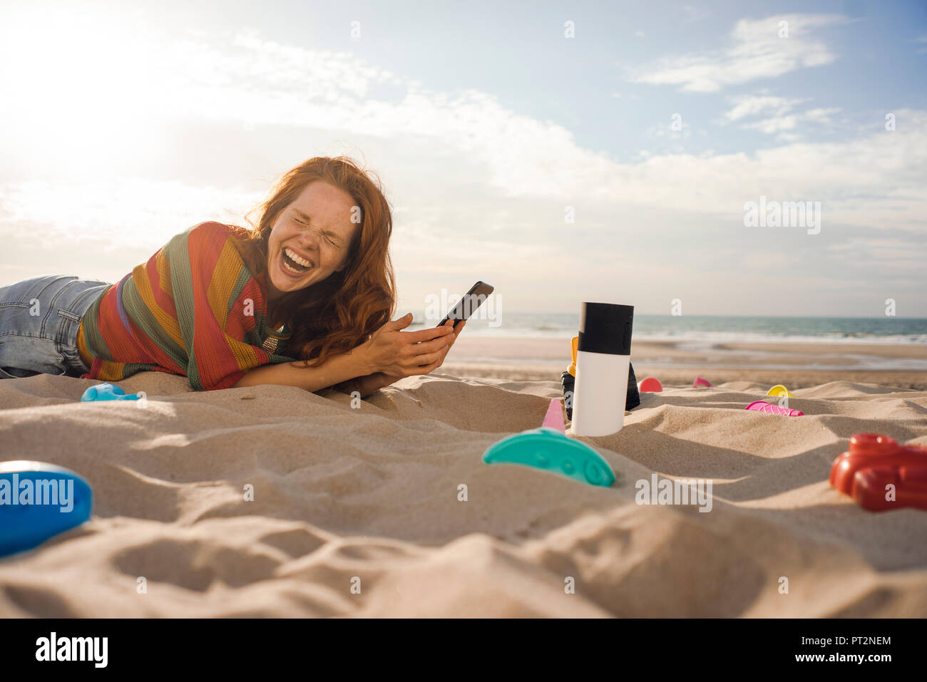 Rothaarige Frau am Strand mit Strand Spielzeug, sie ihr Smartphone Stockfoto