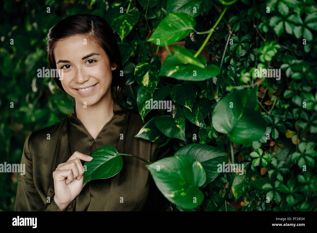 Portrait von lächelnden jungen Frau an der Wand mit Kletterpflanzen Stockfoto