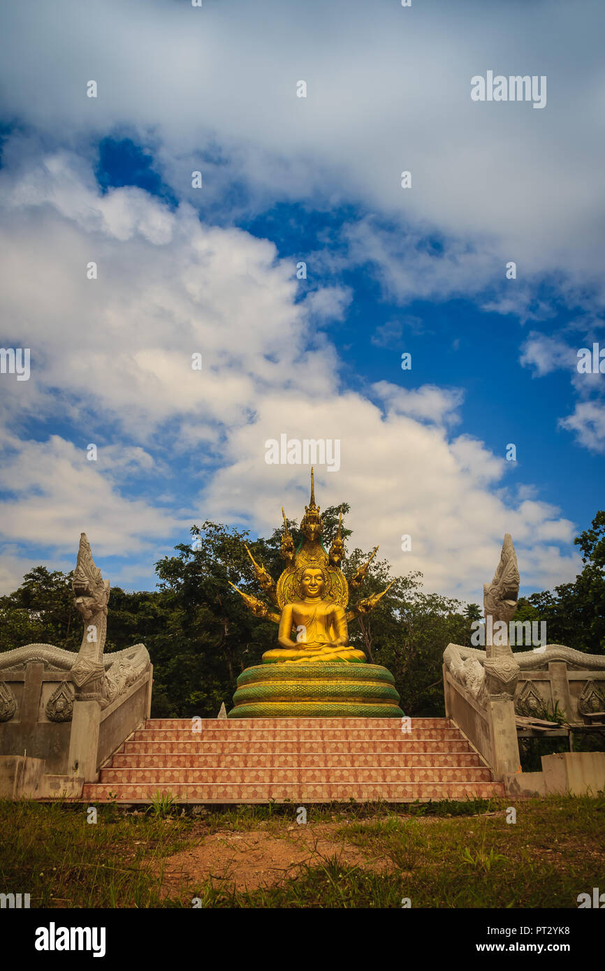 Wunderschöne goldene Buddha Statue mit sieben Phaya Naga Köpfe unter weißen Wolken und blauer Himmel. Outdoor golden sitzender Buddha Bild geschützt durch Stockfoto