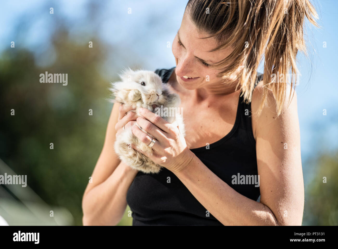 Junge lächelnde Frau mit pelzigen Baby Kaninchen in ihren Händen außerhalb an einem sonnigen Tag. Stockfoto