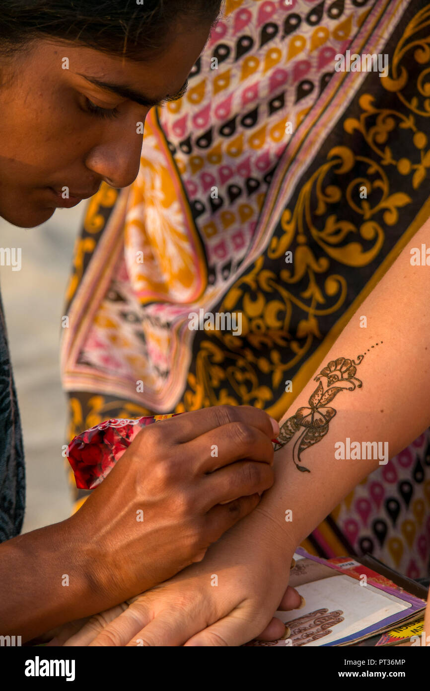 Eine lokale indische Frau Farben henna Färbung auf einem westlichen Touristen arm am Strand. Stockfoto