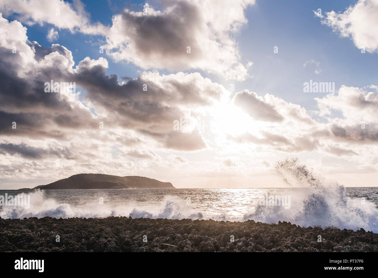 Felsiger Strand mit Welle brechen, Sonne und Wolken spielen, Winter in Griechenland, Insel Proti im Hintergrund Stockfoto