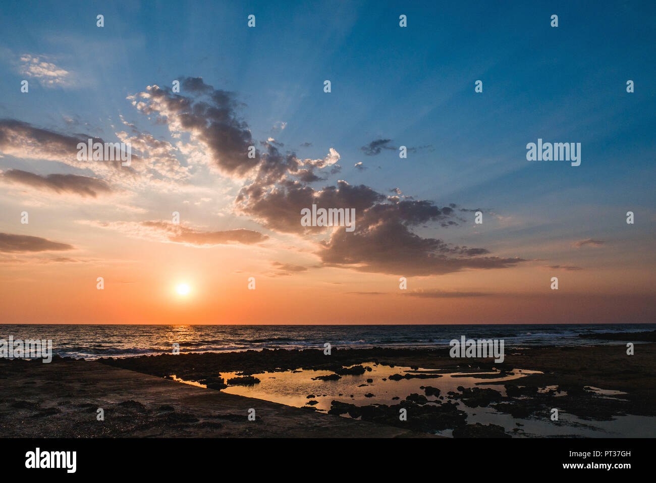 Sonnenuntergang am Meer mit Strand und Wellen und Wolken Stockfoto