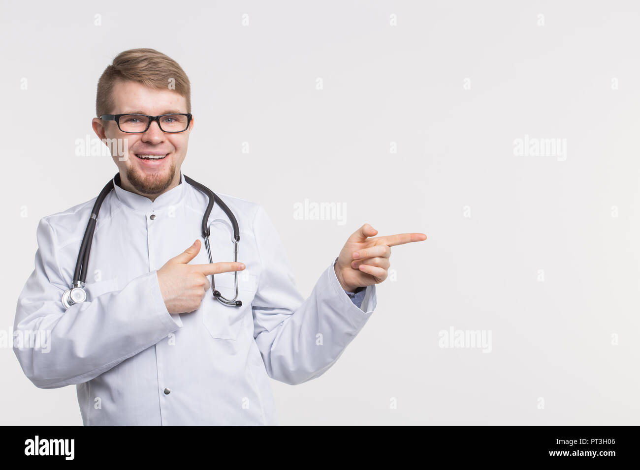Portrait von glücklichen jungen Arzt im Studio mit Stethoskop nach rechts weisender Stockfoto
