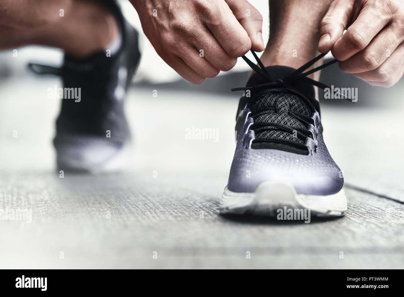 Zugeschnittenes Bild der Hände binden Schnürsenkel auf Sneaker, Lauffläche Hintergrund. Hände von Sportler mit schrittzähler Schnürsenkel binden auf sportliche Sneaker. Ru Stockfoto