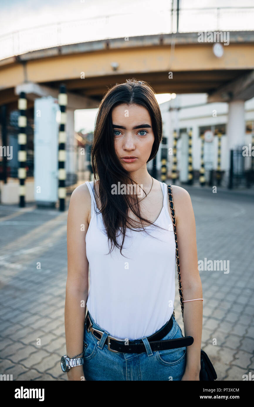Verängstigte junge Frau in Weiß Top und Jeans gekleidet steht unter der Stadt Brücke allein. Jugendlich Mädchen auf Kamera mit einem traurigen Gesichtsausdruck. Stockfoto