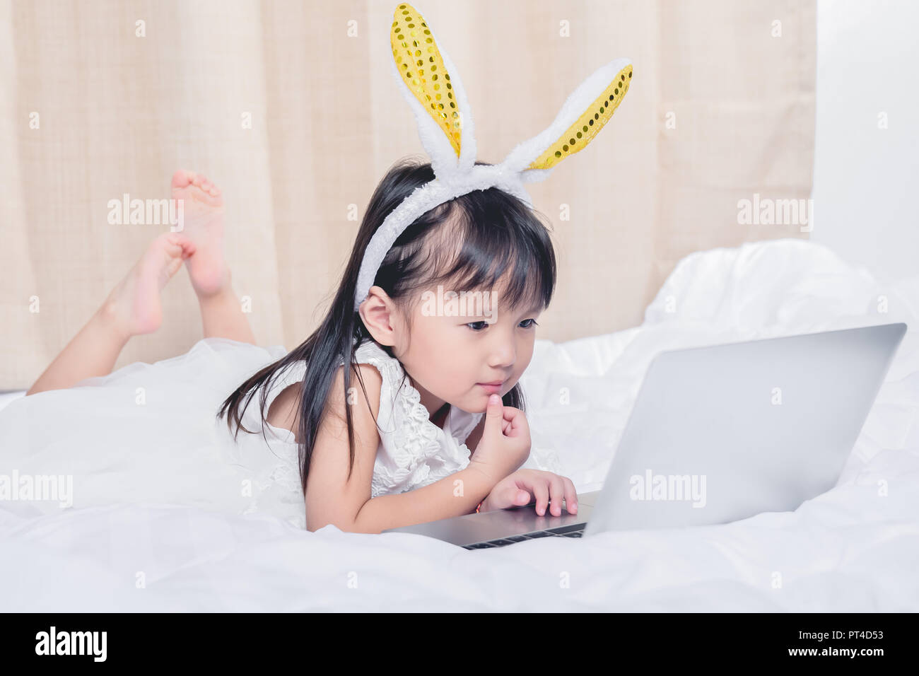Kleines Mädchen liegt mit Laptop auf dem Bett glücklich lächelnd über das Internet ansehen und Spaß haben, in Beziehung mit Technologie Konzept Stockfoto