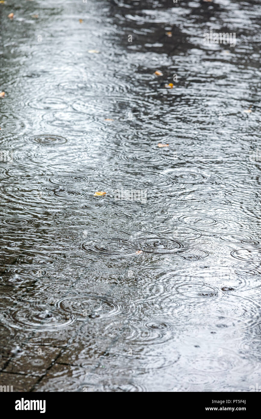 Bürgersteig mit Wasserpfützen bei starkem Regen überflutet. Detailansicht Stockfoto