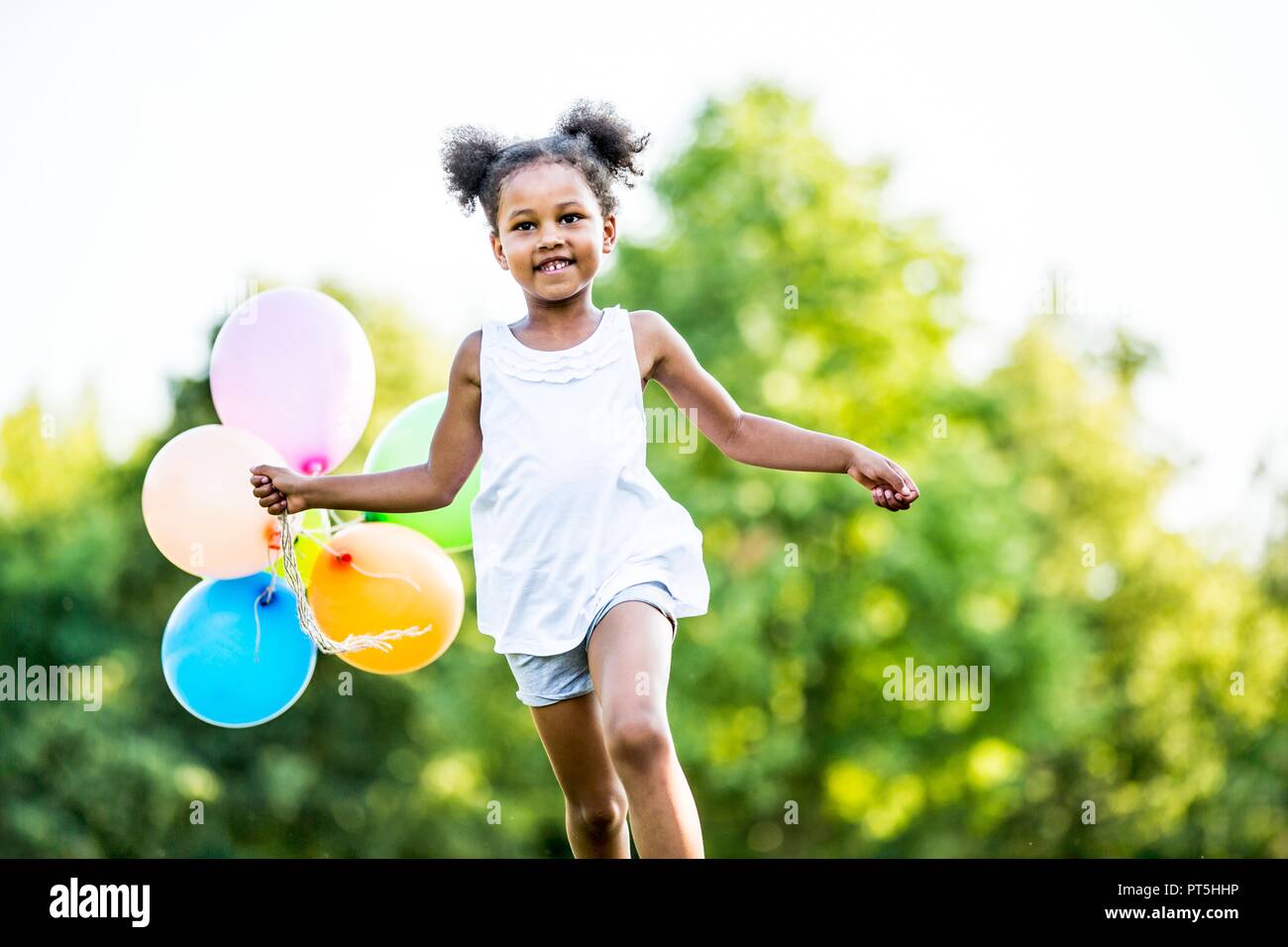 Mädchen in Bündeln mit Luftballons im Park, ein Lächeln auf den Lippen. Stockfoto Mädchen in Bündeln mit Luftballons im Park, ein Lächeln auf den Lippen. Stockfoto