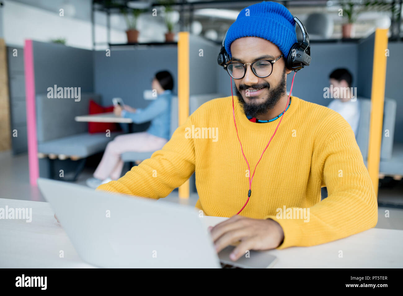 Positive zufrieden aus dem Nahen Osten App Entwickler in Kopfhörer am Tisch sitzen und mit Laptop im Open Space Office arbeiten Stockfoto