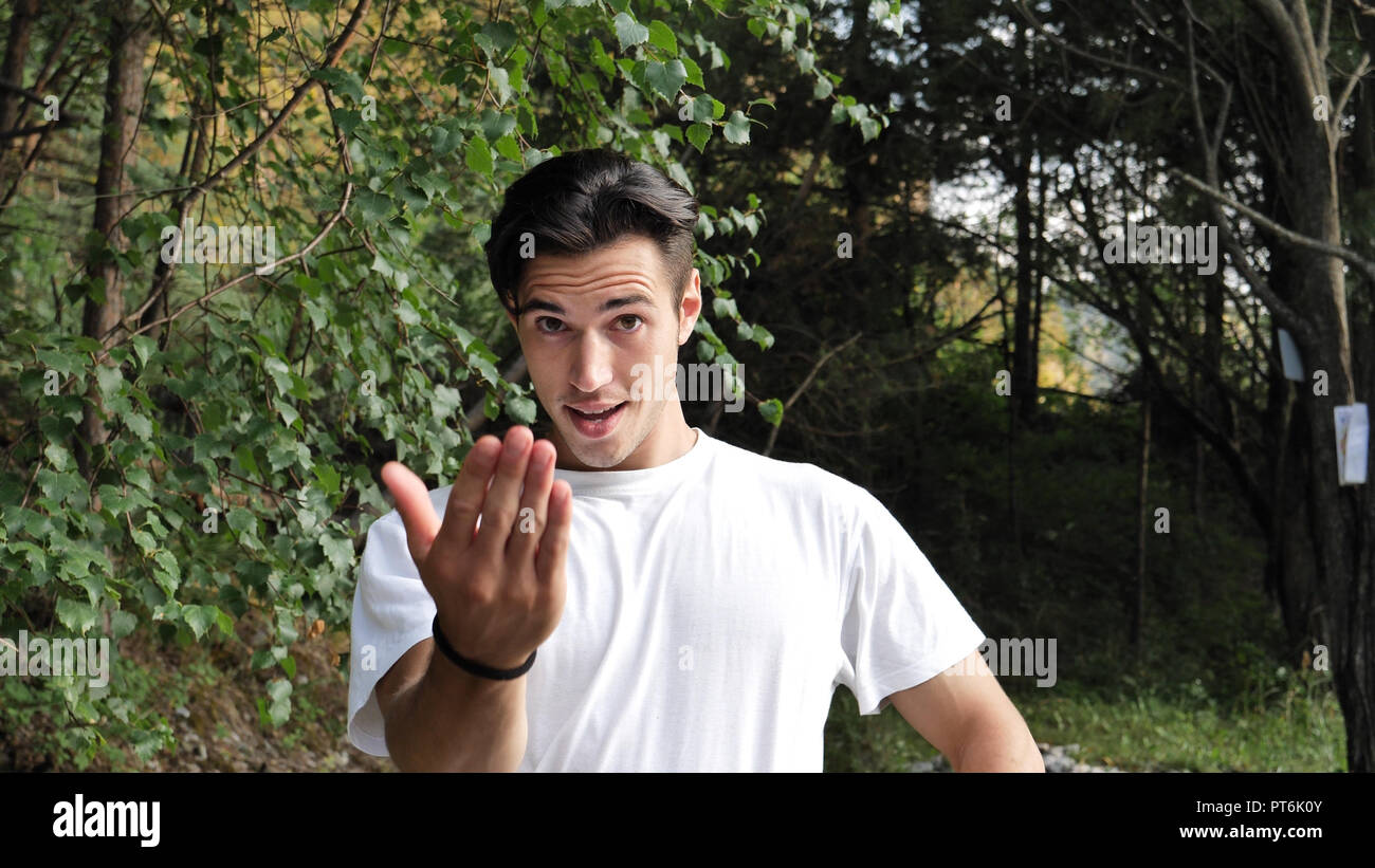 Junge Mann in der Natur bei Anrufen, die näher mit Geste Stockfoto