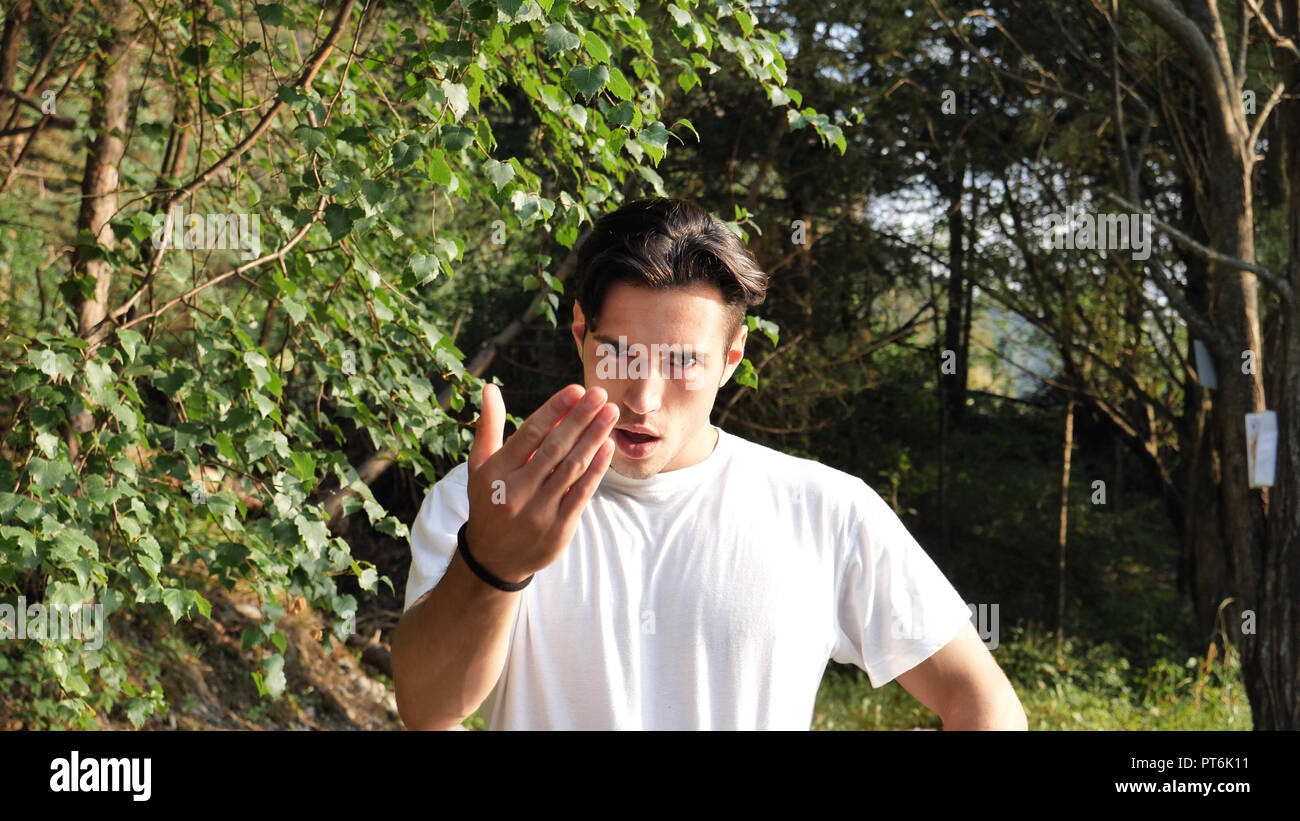 Junge Mann in der Natur bei Anrufen, die näher mit Geste Stockfoto