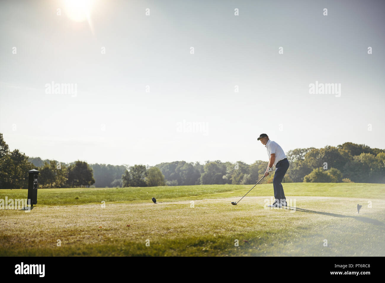 Sportliche älterer Mann über T-Stück weg mit seinem Treiber beim Spielen Sie eine Runde Golf auf einem sonnigen Tag Stockfoto