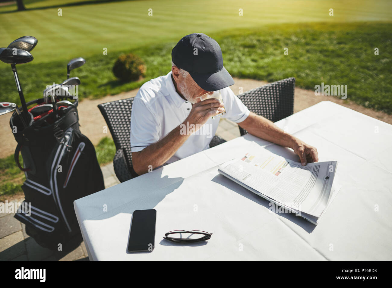 Lächelnd älterer Mann genießen eine Tasse Kaffee und eine Zeitung lesen, während an einem Kurs Restaurant sitzen nach einer Runde Golf Stockfoto