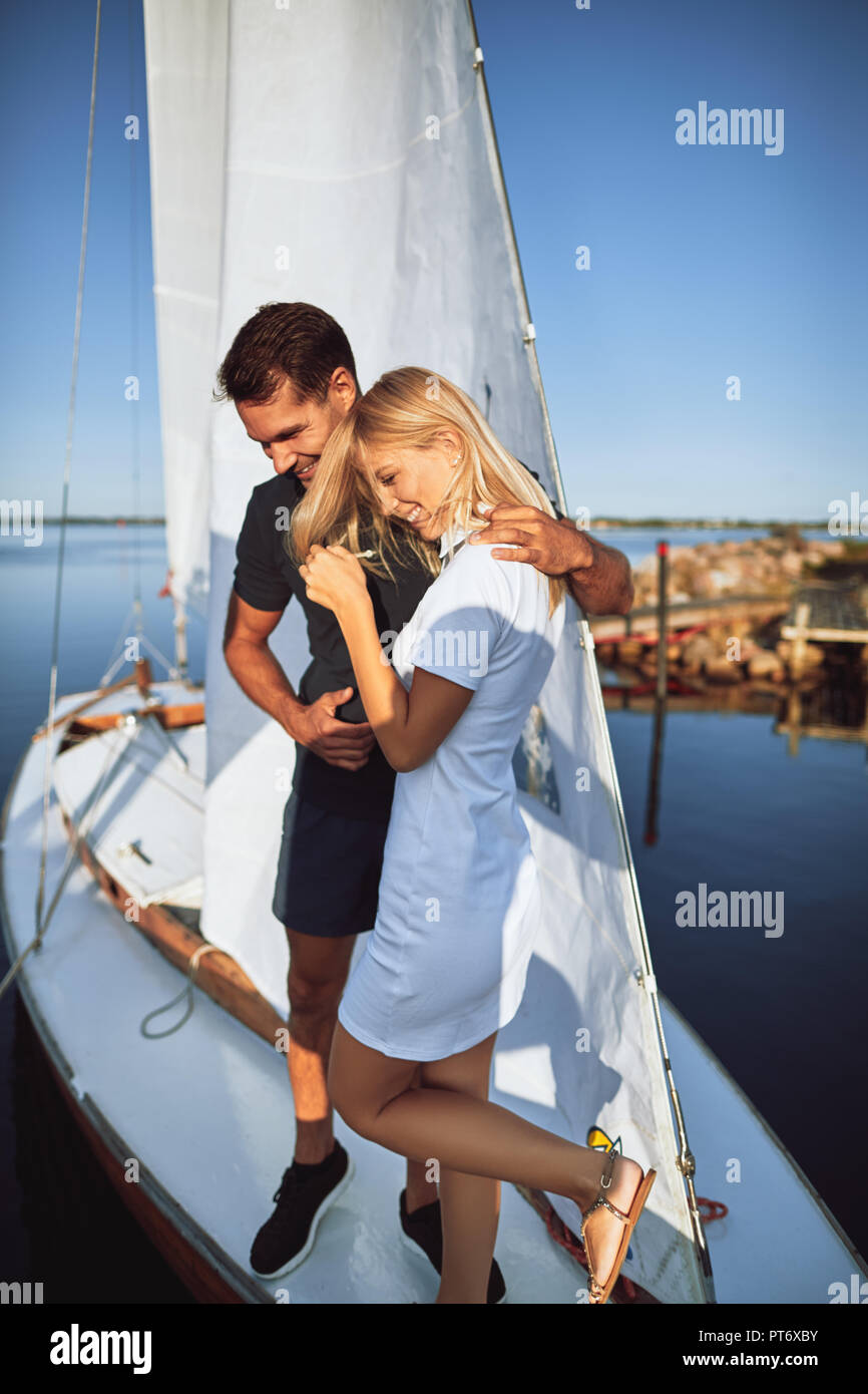 Lachende junge Mann und Frau stehen Arm in Arm zusammen auf dem Deck der Yacht und geniessen Sie einen sonnigen Tag Segeln Stockfoto