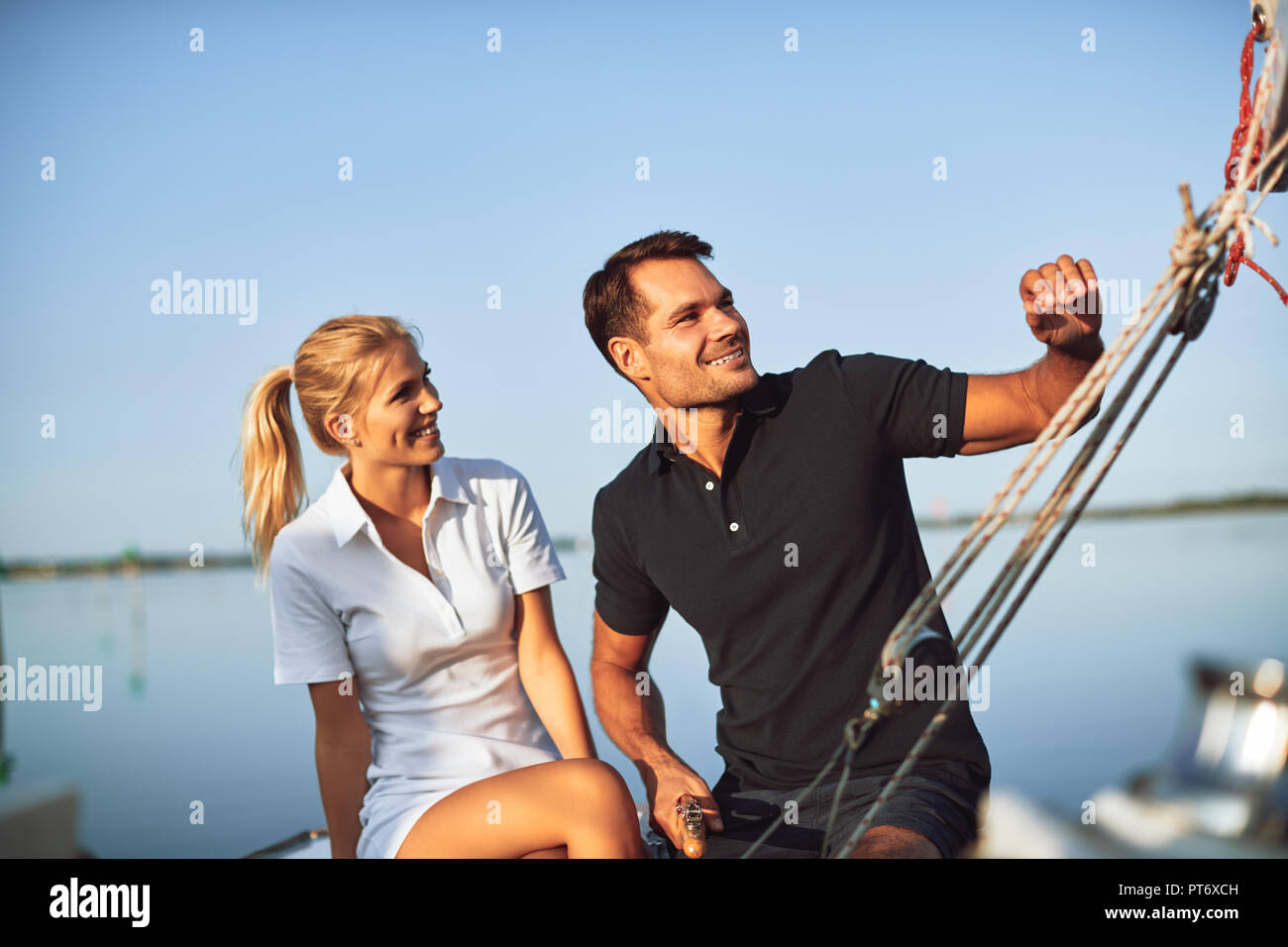 Lächelnde junge Paar genießen Sie einen Nachmittag segeln gemeinsam beim Sitzen auf dem Deck der Yacht Stockfoto