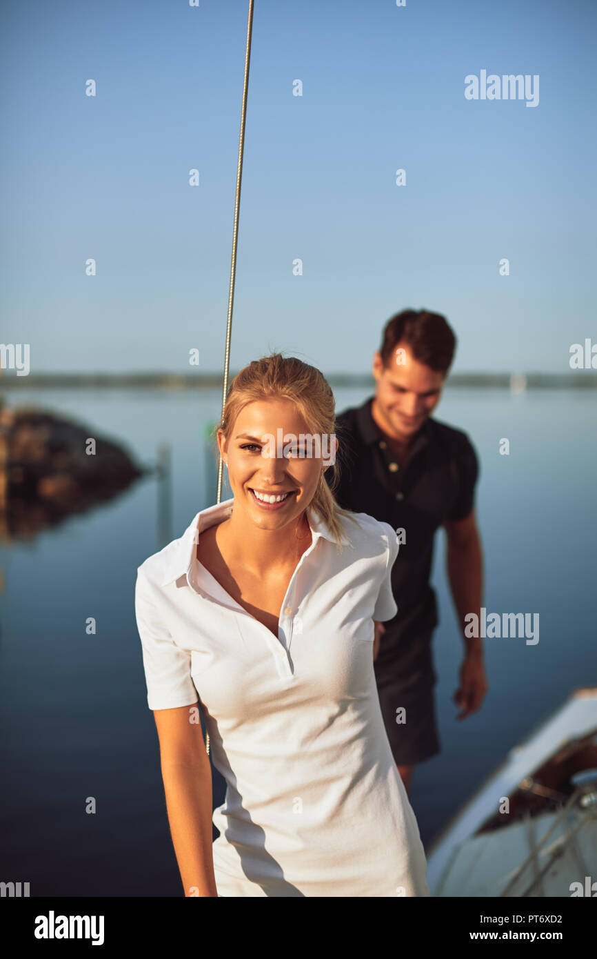 Lächelnde junge Frau, die ihren Mann an der Hand auf dem Deck des Bootes und genießen Sie den Tag gemeinsam Segeln Stockfoto