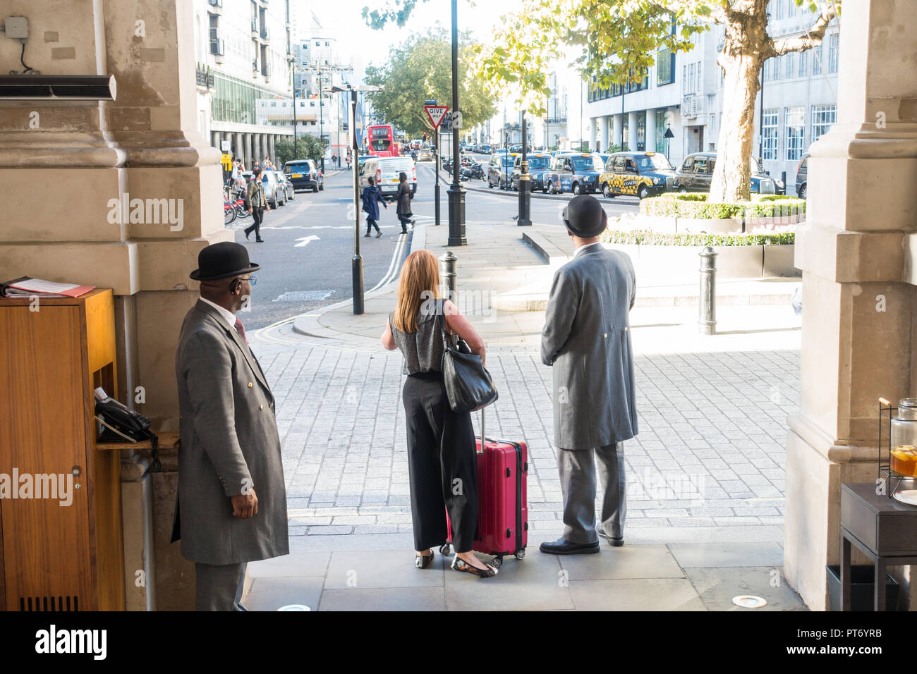 Türsteher tragen Bowler Hüte außerhalb des Langham Hotel mit einem weiblichen Gast für ein Taxi, London, UK, Europa warten. Stockfoto