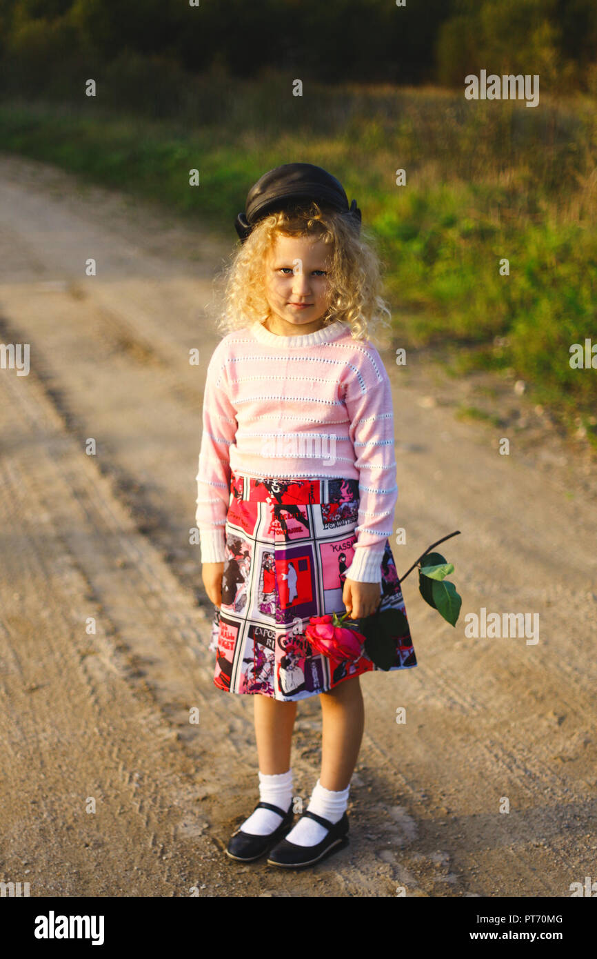 Kleine lockige blonde Mädchen mit Blumen auf der Straße Stockfoto