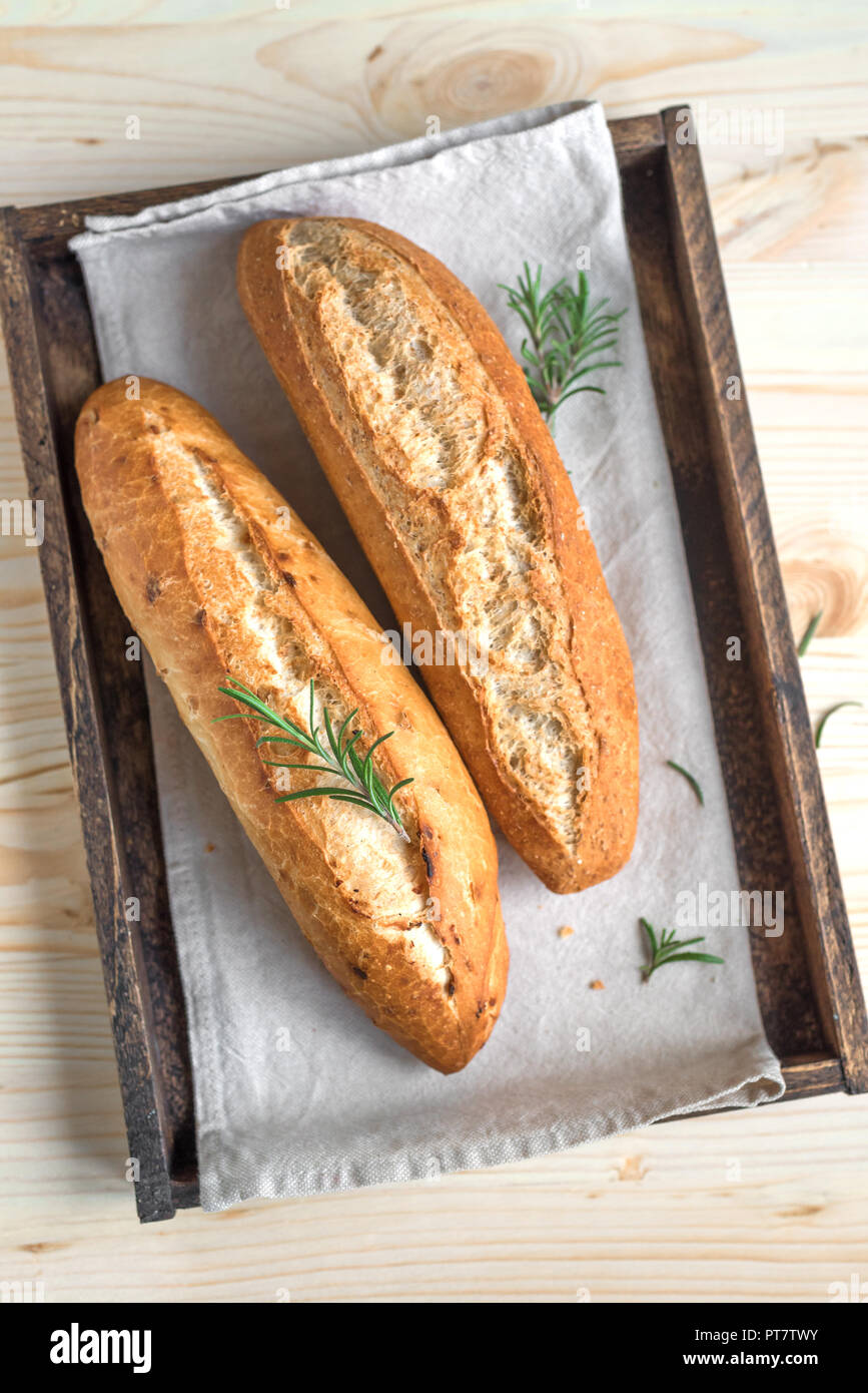 Frische hausgemachte Brot mit Rosmarin in rustikalen Holzmöbeln, Ansicht von oben. Sourdough mini Baguette. Stockfoto
