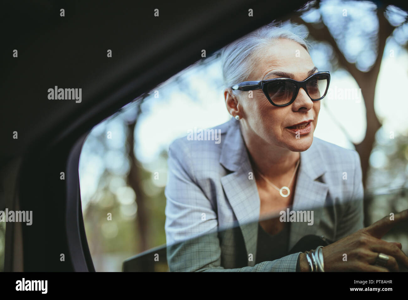 Schöne ältere Frau im Gespräch mit dem Taxifahrer durch geöffnete Fenster. Bei Sonnenbrillen im Gespräch mit Cab Driver Geschäftsfrau. Stockfoto