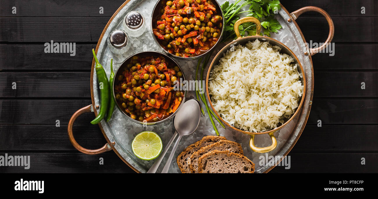 Banner von vegan Curry mit grünen Erbsen und Basmatireis auf einem hölzernen Tisch Tablett serviert, gesunde indische Speisen Stockfoto