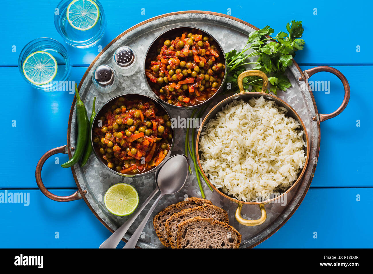 Vegan curry mit grünen Erbsen und Basmatireis auf einem blauen Tisch Tablett serviert, gesunde indische Speisen und Limonade in Gläsern Stockfoto