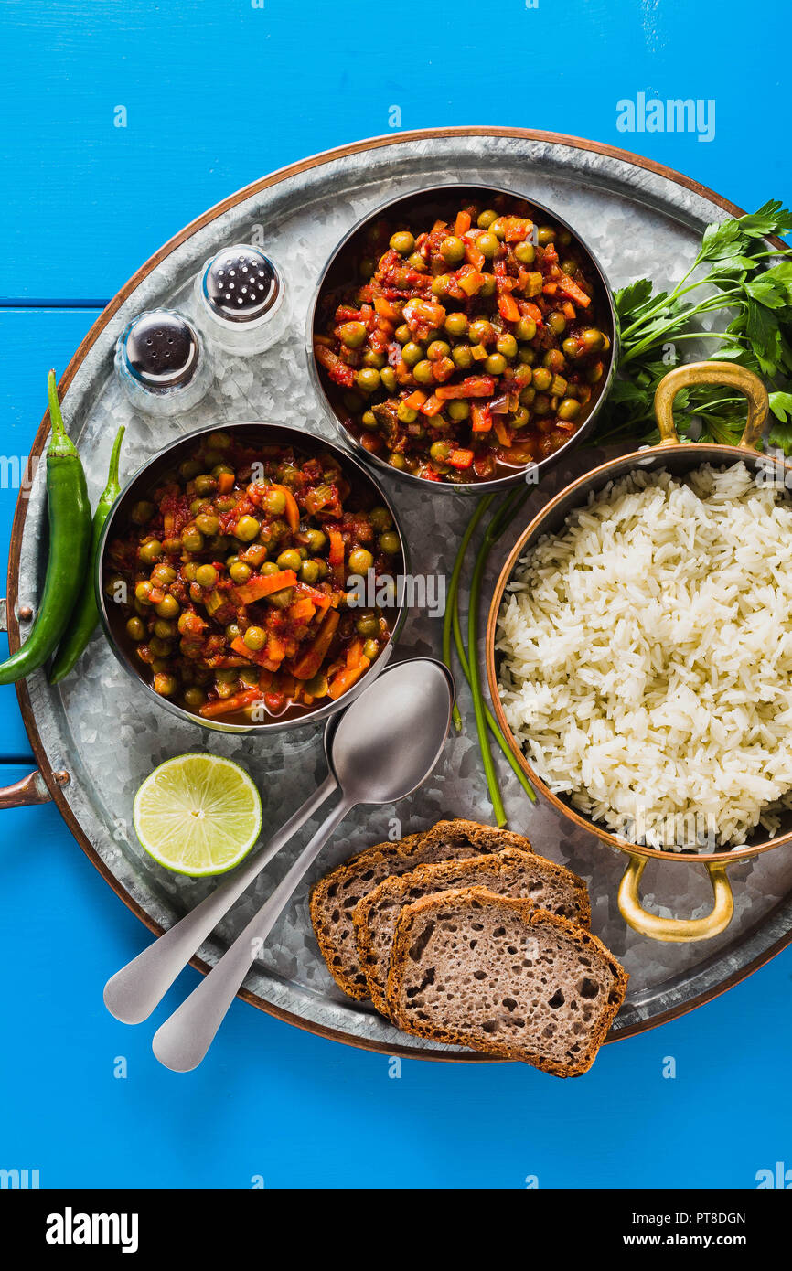 Vegan curry mit grünen Erbsen und Basmatireis auf einem blauen Tisch Tablett serviert, gesunde indische Speisen Stockfoto