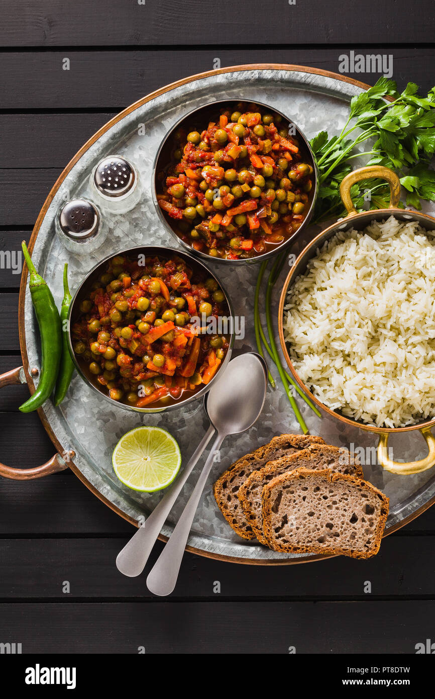 Vegan curry mit grünen Erbsen und Basmatireis auf einem hölzernen Tisch Tablett serviert, gesunde indische Speisen Stockfoto