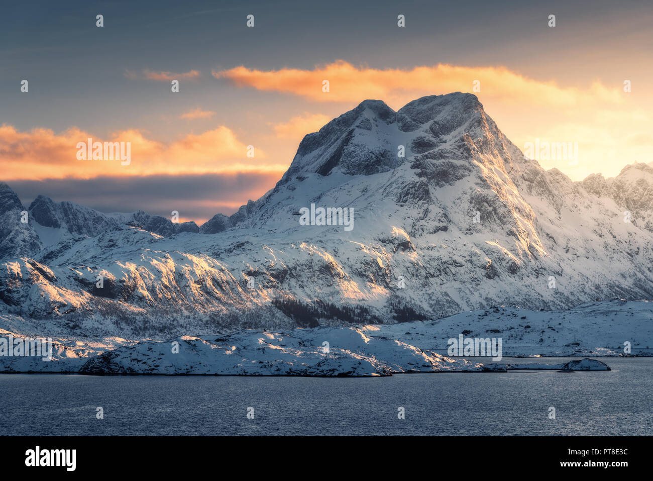 Majestic Szene mit schönen hohen schneebedeckten Berge bei Sonnenuntergang im Winter. Lofoten, Norwegen. Landschaft mit schneebedeckten Felsen, Meer, orange sky wi Stockfoto