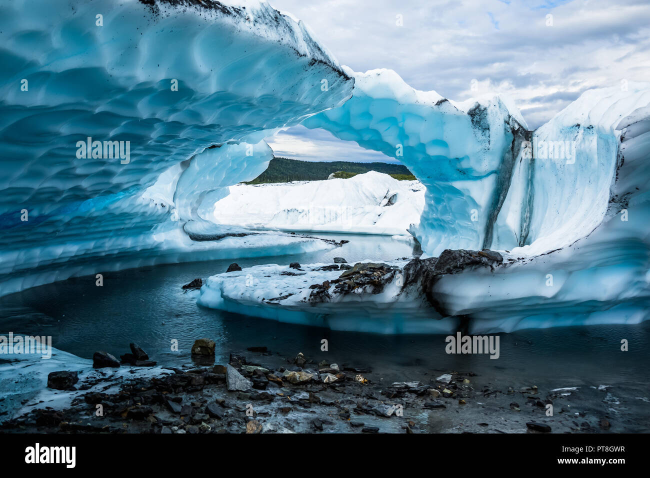 Aus einem schmalen, gewundenen Fluss von Schmelzwasser auf der Matanuska Gletscher geschnitzten mehrere große Flossen der überhängenden Eis. Die Schichten der Flossen Erscheinen einen Bogen zu bilden Stockfoto